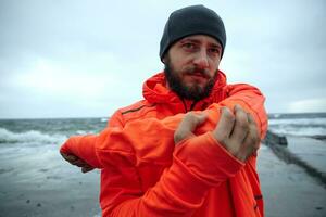 portrait de Jeune sévère brunette Masculin avec luxuriant barbe Faire réchauffer avant Matin courir à bord de mer, à la recherche pensivement devant avec plié lèvres. aptitude Masculin modèle photo