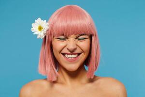 portrait de Jeune magnifique rose aux cheveux femme avec bob la Coupe de cheveux montrant sa parfait blanc les dents tandis que souriant Heureusement avec fermé yeux, isolé plus de bleu Contexte photo