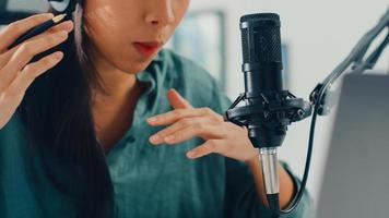 une fille asiatique heureuse enregistre un podcast sur son ordinateur portable avec des écouteurs et un microphone parle avec le public dans sa chambre. une podcasteuse crée un podcast audio depuis son home studio, reste à la maison concept. photo