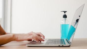 femme asiatique utilisant un gel désinfectant à l'alcool se laver les mains avant de travailler sur un ordinateur portable pour protéger le coronavirus. les femmes poussent l'alcool à nettoyer pour l'hygiène lorsque la distanciation sociale reste à la maison et le temps d'auto-quarantaine.