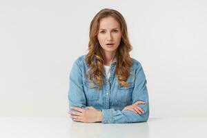 ute désapprobation Jeune femme séance à le tableau, avec longue blond ondulé cheveux, portant une denim chemise, entendu mal nouvelles. à la recherche à le caméra isolé plus de blanc Contexte. photo