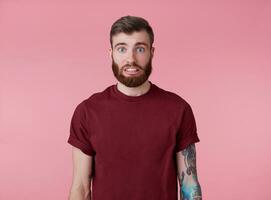 oups quelque chose faux portrait de Jeune attrayant tatoué rouge barbu homme dans Vide T-shirt, regards Pardon et triste, des stands plus de rose Contexte. photo