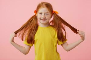 content menue taches de rousseur roux fille prend le sien deux queues, largement souriant et regards mignon, porte dans Jaune T-shirt, des stands plus de rose Contexte. photo