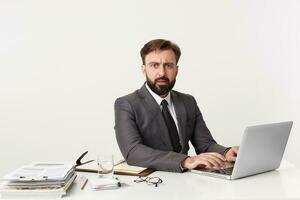 portrait de un indigné Bureau Haut directeur qui a été distraits de travail, séance à bureau dans bureau, travail pour le sien portable , habillé dans un coûteux costume avec une cravate. photo