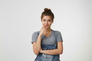 magnifique fille regards dans le distance debout, elle tête légèrement levée, main franchi doigt sur une lèvres, pense à propos avenir, fait du des plans, rêves, se sent sur de soi dans capacités, isolé plus de blanc Contexte photo