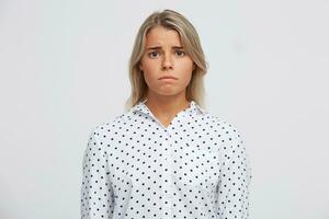 fermer de triste déprimé blond Jeune femme porte polka point chemise se sent dérangé et déçu isolé plus de blanc Contexte regards directement dans caméra photo