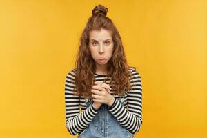 intérieur portrait de Jeune mécontent gingembre filles, garde sa paumes ensemble, courbes sa lèvres avec une triste faciale expression. isolé plus de Jaune Contexte. photo