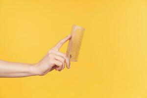 studio photo de Jeune femme main avec Naturel manucure en gardant brosse à cheveux dans il tandis que posant plus de Orange arrière-plan, Aller à faire coiffure avant Aller en dehors