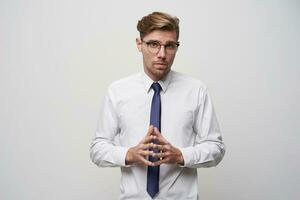 une Jeune homme des stands avec le sien les doigts plié dans devant, parlant à le sien chef, donnant lui une rapport ou présentation. regards par lunettes, une peu ringard, tendu, sur une blanc Contexte photo