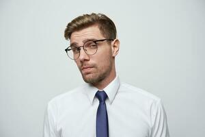 le Jeune homme regards par le sien des lunettes incrédule, évaluatif, pense Comment beaucoup il pouvez confiance, est il lucratif pratique, fait du une décision évaluer le des risques, isolé plus de blanc Contexte photo