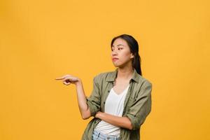 une jeune femme asiatique montre quelque chose d'étonnant dans un espace vide avec une expression négative, des cris excités, des pleurs émotionnels en colère dans des vêtements décontractés isolés sur fond jaune. concept d'expression faciale. photo