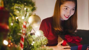 jeune femme asiatique utilisant un appel vidéo sur tablette parlant avec un couple avec une boîte de cadeau de Noël, un arbre de noël décoré d'ornements dans le salon à la maison. nuit de noël et festival de vacances du nouvel an. photo