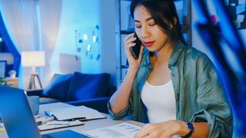 femmes asiatiques indépendantes utilisant un ordinateur portable parlant au téléphone entrepreneur occupé travaillant à distance dans le salon. travailler à partir de la surcharge de la maison la nuit, travail à distance, distanciation sociale, quarantaine pour le coronavirus.