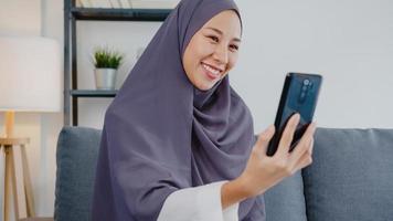 une dame musulmane d'asie porte le hijab à l'aide d'un appel vidéo téléphonique parlant avec un couple à la maison. jeune adolescent faisant une vidéo vlog sur les réseaux sociaux sur un canapé dans le salon. distanciation sociale, quarantaine pour le virus corona. photo