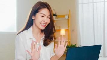 jeune femme d'affaires asiatique utilisant un appel vidéo pour ordinateur portable parlant avec un couple tout en travaillant à domicile dans le salon. auto-isolement, distanciation sociale, quarantaine pour le coronavirus dans le prochain concept normal.