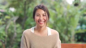 femme asiatique se sentant heureuse en souriant et en regardant la caméra tout en se relaxant sur la table dans le jardin à la maison le matin. les femmes de style de vie se détendent à la maison concept. photo