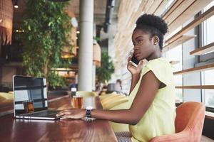 jeune belle femme d'affaires afro-américaine parlant au téléphone tout en travaillant dans un café photo