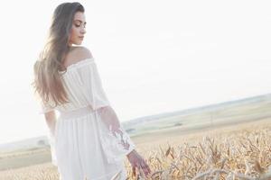 belle fille en robe blanche s'exécutant sur le champ de blé d'automne au coucher du soleil photo