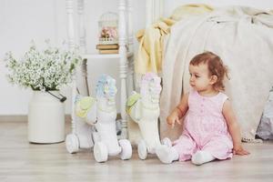 belle petite fille jouant des jouets. blonde aux yeux bleus. chaise blanche. la Chambre des enfants. portrait de petite fille heureuse. concept d'enfance photo