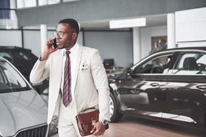 jeune homme d'affaires noir sur fond de salon automobile. concept de vente et de location de voiture photo