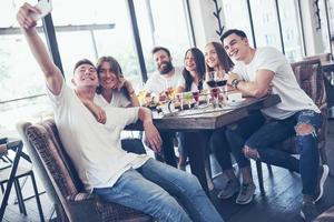 un groupe de personnes fait une photo de selfie dans un café. les meilleurs amis se sont réunis à une table pour manger des pizzas et chanter diverses boissons