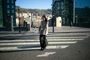 brunette exécutif femme dans une gris manteau, traversée une route avec sa travail valise. photo