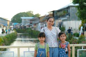 mère et les enfants pose souriant et à la recherche à le caméra sur le pont plus de le rivière. khlong mae kha, une Nouveau attraction dans chiang Mai, Thaïlande. photo