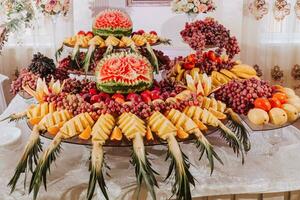 table avec divers fruit décorations. pastèque sculpture, ananas tranches, raisins, Orange photo