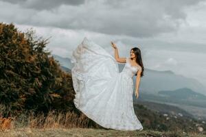 magnifique la mariée contre le Contexte de l'automne montagnes dans devant. une luxueux blanc robe flotte. mariage la cérémonie sur Haut de le Montagne. gratuit espace. photo