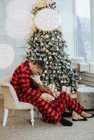 Jeune magnifique couple dans correspondant à rouge pyjamas près le Noël arbre. joie, câlins et bisous. Nouveau années vacances et cadeaux en dessous de le Noël arbre photo