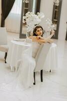 portrait de une magnifique fille dans une mariage robe. le la mariée dans une luxueux robe, séance sur une chaise. verticale photo