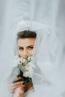le la mariée pose avec une bouquet, couvert avec une voile. une les filles vue par une voile. mariage robe. mariage portrait photo