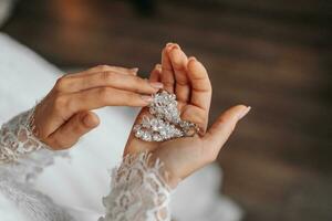 détails. mariage accessoires. la mariée détient cristal des boucles d'oreilles dans mains, tondu photo. magnifique mains photo