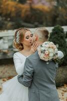 le jeune marié embrasse le la mariée et baisers son, le la mariée regards à le jeune marié. mariage marcher dans le jardin photo