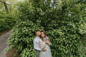 la mariée et jeune marié supporter sur une Contexte de vert feuilles. le jeune marié baisers le la mariée sur le temple photo