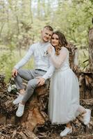 doux embrasse de le la mariée et jeune marié dans le forêt. le jeune marié est habillé dans une blanc chemise et gris pantalon, le la mariée est dans une lumière blanc robe photo