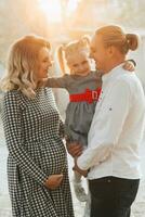 Jeune Enceinte femme avec famille à le coucher du soleil dans le parc photo