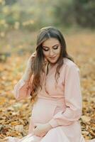 portrait de une Jeune Enceinte femme séance sur une jauni l'automne feuille photo