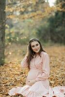 portrait de une Jeune Enceinte femme séance sur une jauni l'automne feuille photo