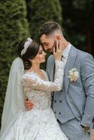 européen mariage couple dans le parc. le la mariée dans une magnifique robe avec manches et une couronne sur sa diriger. jeune marié avec une noir barbe de caucasien apparence dans une classique costume photo