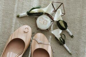 le de la mariée mariage des chaussures sont beige, là sont Trois calla fleur boutonnières et mariage anneaux dans une verre boîte photo