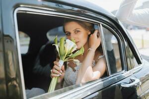mariage portrait, une photo de une élégant la mariée avec une bouquet de fleurs dans le fenêtre de une noir rétro voiture