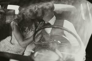 une luxueux et élégant mariage couple tendrement embrasse dans le milieu de une élégant rétro auto. le photo a été pris par le pare-brise. magnifique la mariée et Beau jeune marié dans rétro style.