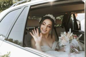 le la mariée est assis dans une blanc luxe voiture sur le mariage journée avec une bouquet. portrait de le la mariée. luxuriant blanc dentelle robe. photo