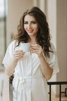 côté vue de Jeune femme dans peignoir de bain permanent sur Hôtel balcon profiter vue avec tasse de café, bien matin, sentiment positif, optimiste, Nouveau ensoleillé journée photo