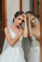 le la mariée dans une mariage robe avec une longue train et une voile des stands près une verre cas. de face photo