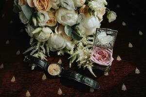 photo de mariage accessoires. luxueux bouquet de le jeune marié. or anneaux sur une supporter avec fleurs, une noir classique regarder sur une Bourgogne Contexte.