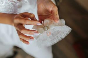 jarretière sur le jambe de le la mariée dans sa mains, fermer. Matin de le la mariée photo