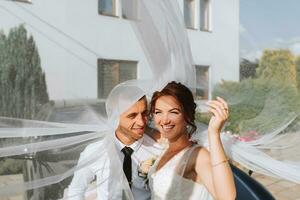 mariage portrait. le la mariée et jeune marié embrassé, couvert se avec une voile, et Cordialement sourit. vacances concept. photo