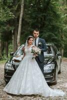 de face vue de une marié la mariée et jeune marié portant de fête vêtements permanent contre une noir voiture sur leur mariage journée photo